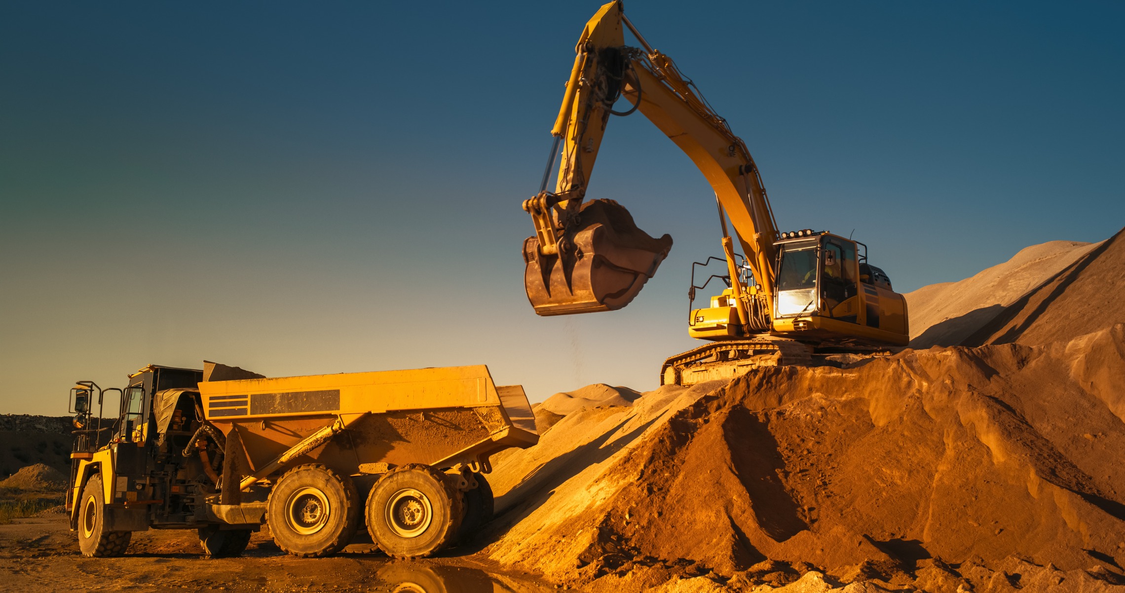 Tiefbau im Fokus: Lösungen für komplexe Risiken Das Bild zeigt einen Bagger, der auf einem Sandberg steht und Sand in einen LKW schaufelt.